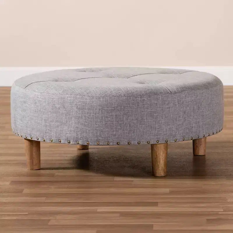 Pouf rotondo rivestito in tessuto, con parte superiore trapuntata e borchie decorative